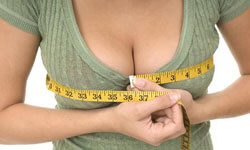 Picture of a woman, happy with her perfect breast reduction procedure she had with Top Plastic Surgeons in beautiful Cancun, Mexico.  The woman is facing the camera, measuring her breasts with a tape measure, and wearing an olive colored blouse