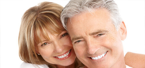 Close-up picture of a smiling couple looking directly into the camera showing their happiness with the plastic surgery they had done in Cancun, Mexico.  The woman has medium brown hair and the man has white hair.