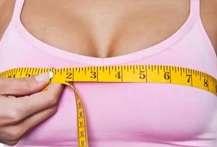 Picture of a woman measuring her breasts with a tape measure, and happy with the perfect breast reduction procedure she had with top plastic surgeons in beautiful Cancun, Mexico.  She is wearing a light purple top and facing the camera.