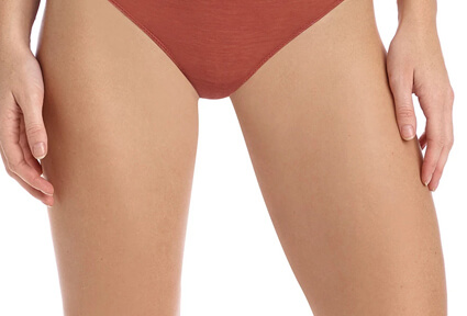 Picture of a trim woman wearing a red bikini bottom, and happy with her perfect thigh lift she had with top plastic surgeons in beautiful Cancun, Mexico.  The woman is facing the camera with both arms down to her sides.