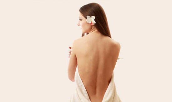 Picture of a woman sitting with her back to the camera and happy with her perfect back liposuction procedure she had with Cancun MedVentures in beautiful Cancun, Mexico.  The woman has a white towel draped around her.