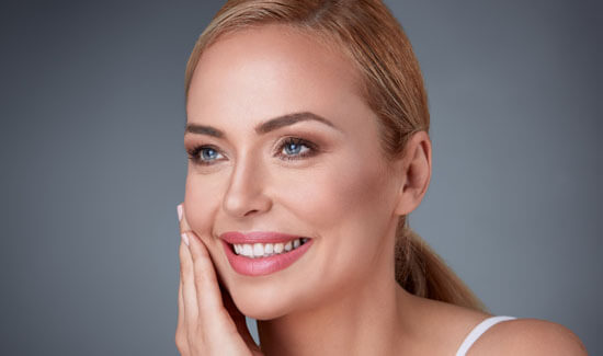 Picture of a smiling woman, facing slightly to the side of the camera and happy with her perfect face lift procedure she had with Cancun MedVentures in beautiful Cancun, Mexico.  The woman has her hand to the side of her face indicating her happiness with the face lift.